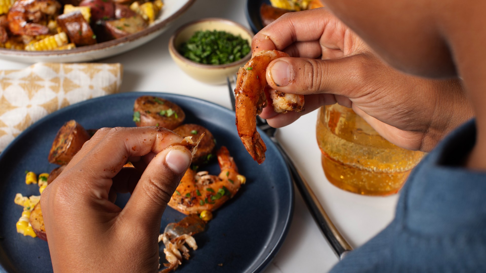 A boy holding pieces of shrimp in his hands above a plate of shrimp